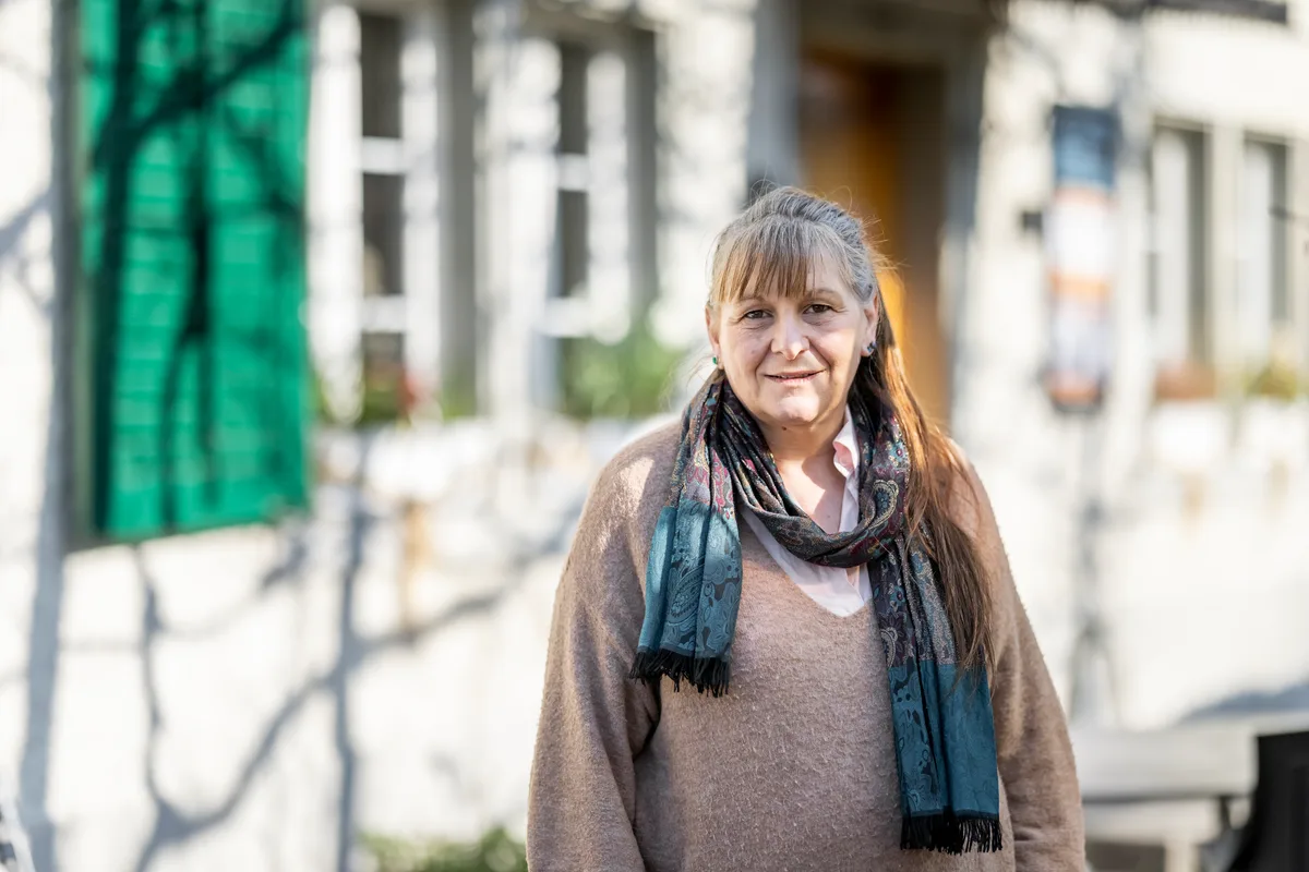 Frau mittleren Alters mit einem braunen Pullover und einem bunten Schal.